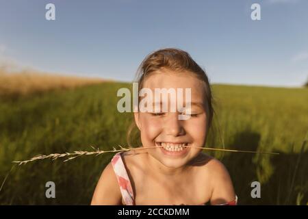 Close-up of smiling girl with eyes closed sitting on land against clear sky during sunset Stock Photo