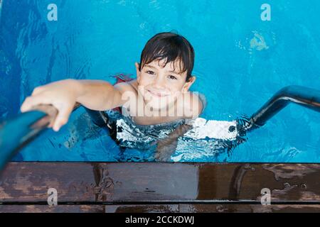 Smiling boy holding ladder while standing in swimming Pool