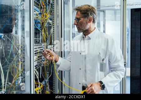 Mature man plugging transceiver on fiber optic cable into rack Stock Photo