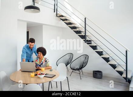 Multi-ethnic couple using laptop at dining table in modern penthouse Stock Photo