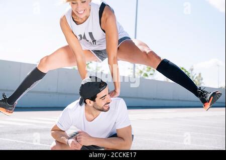 Smiling woman jumping over man on street against sky during sunny day Stock Photo