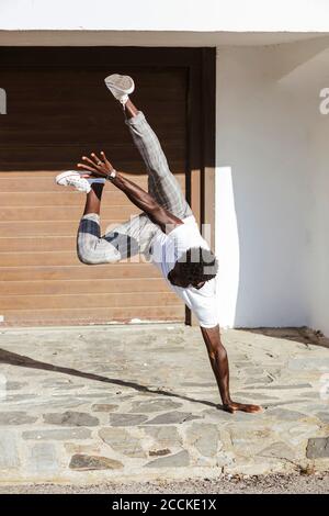Young man doing handstand on footpath during sunny day Stock Photo
