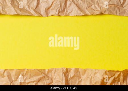 Torn crumpled recycled brown paper on yellow colored paper background inside Stock Photo