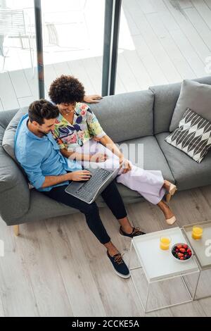 Multi-ethnic couple using laptop while sitting on sofa in penthouse Stock Photo