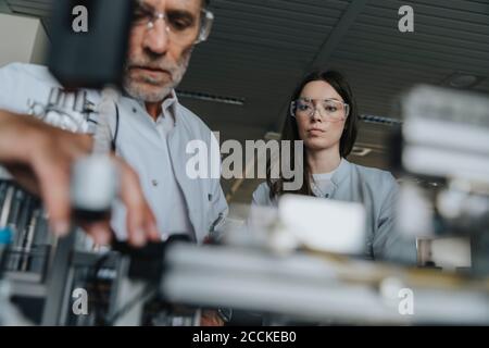 Male and female scientists with protective eyewear examining machine in laboratory Stock Photo