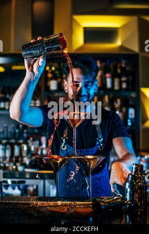 Smiling male bartender pouring alcohol in glasses on bar counter at pub Stock Photo