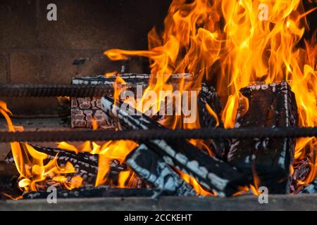 Transparent bright orange flame on charred wood turned to gray ash on a black smoky brick wall of a barbecue oven for kebab on an open fire. Warm, coz Stock Photo