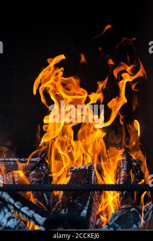 The charred wood in the stove in bright tongues of orange, yellow and red flames against the black background of the smoky wall behind the iron rods o Stock Photo