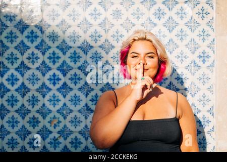 Woman showing silence sign with finger on lips against wall Stock Photo