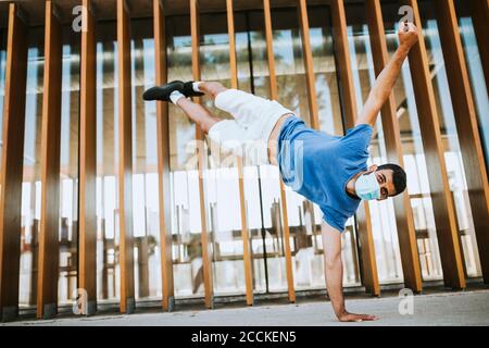 Young man wearing mask doing handstand against built structure Stock Photo