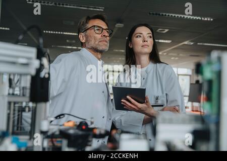 Thoughtful male and female engineers looking away while standing by machinery in laboratory Stock Photo