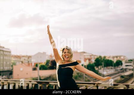 Excited young woman standing with arms outstretched in city Stock Photo