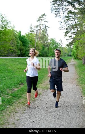 Happy couple jogging on dirt road against trees in forest Stock Photo