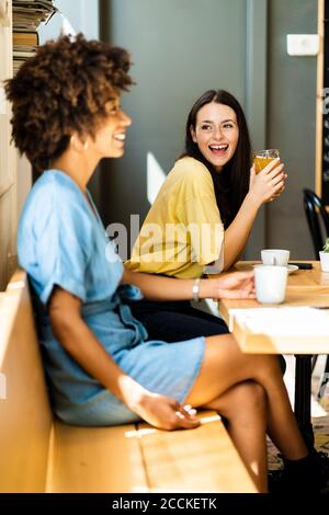 Cheerful woman holding drink while looking friend in cafe Stock Photo
