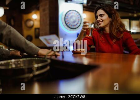 Smiling beautiful woman holding beer glass talking with bartender in restaurant Stock Photo