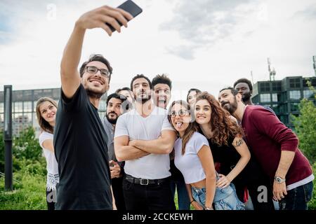 Cheerful man taking selfie with group of friends in park against sky Stock Photo
