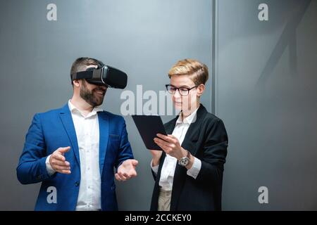 Female entrepreneur using digital tablet while analyzing colleague experiencing virtual reality simulation at office Stock Photo