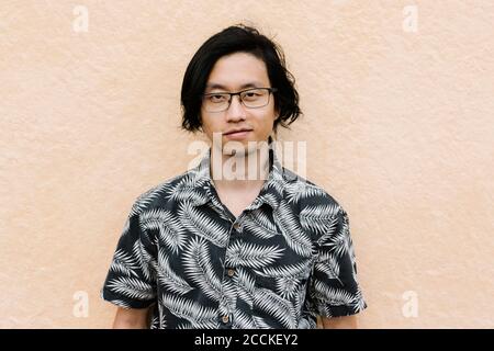 Confident young man wearing eyeglasses standing against wall in city Stock Photo