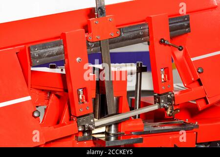 The sharp teeth of the band saw on the modern red metal working machine ensure high cutting accuracy thanks to the adjusting line. Close-up. Stock Photo