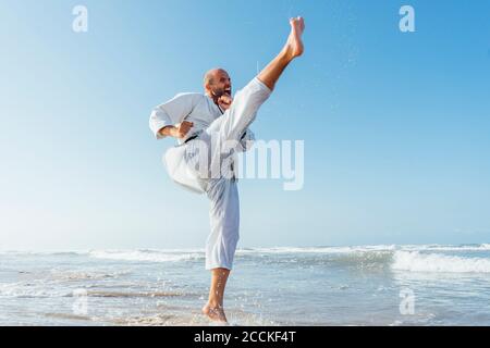 Man screaming while practicing karate in sea against clear sky Stock Photo