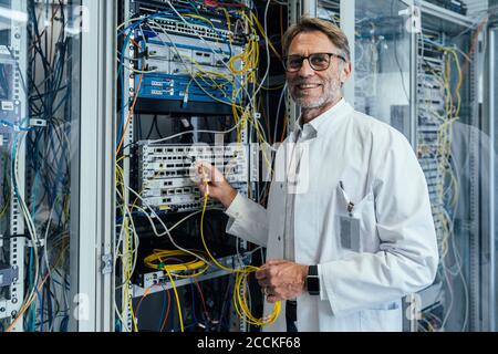 Smiling mature man plugging transceiver on fiber optic cable in data center Stock Photo