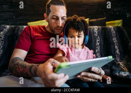 Father with daughter using digital tablet while sitting on sofa at home Stock Photo