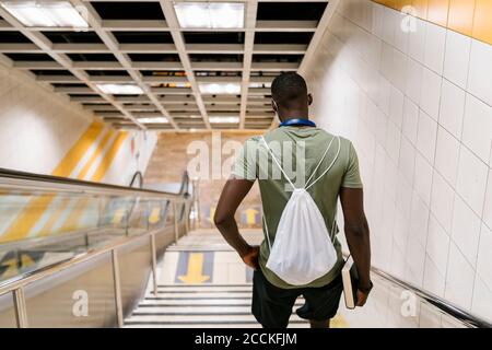 Young man with backpack moving down on steps in subway station