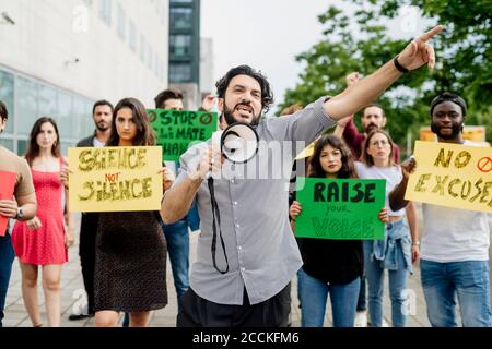 Man screaming through megaphone while protesting with people on street Stock Photo