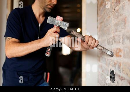 Construction worker using hammer and chisel at a brick wall Stock Photo