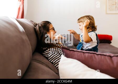 Happy mother and daughter talking while relaxing on sofa at home Stock Photo