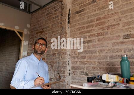 Architect holding clipboard at brick wall in a house under construction Stock Photo