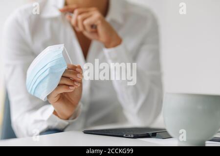 Close-up of businesswoman holding mask at desk in home office Stock Photo