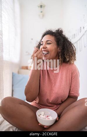 Happy young woman eating strawberries with cream while sitting at home Stock Photo