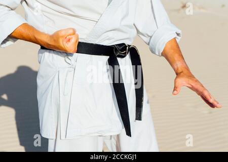 Close-up of mature man practicing karate while standing at beach Stock Photo