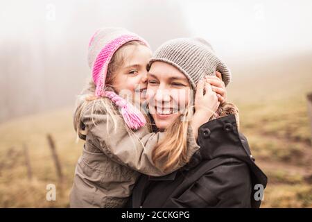 Mother and daughter hugging and laughing in foggy landscape Stock Photo