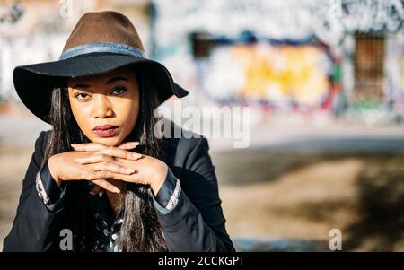Beautiful woman wearing hat with hands clasped sitting outdoors Stock Photo
