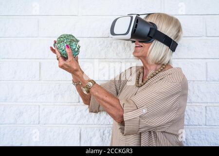 Senior woman holding conch, using virtual reality simulator Stock Photo
