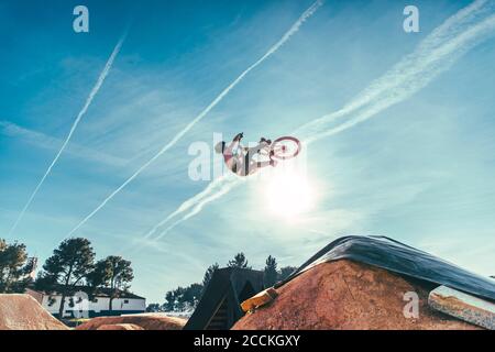 Carefree young man performing stunt with bicycle against blue sky at park during sunset Stock Photo