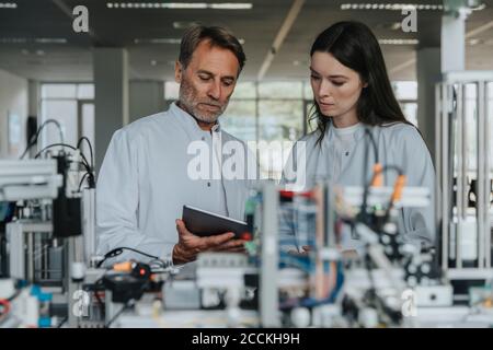 Colleagues discussing over digital tablet while standing by machinery in laboratory Stock Photo