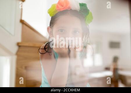 Close-up of cute girl wearing colorful tiara looking through glass at home Stock Photo