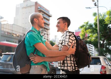 Gay couple with backpacks greeting while standing in city Stock Photo