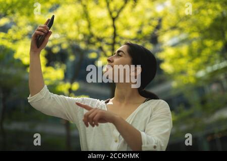 Young woman taking selfie through smartphone against trees Stock Photo