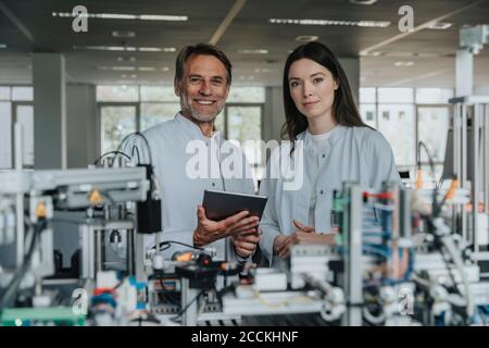 Confident engineers standing by machinery in laboratory Stock Photo