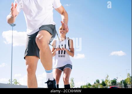 Smiling woman holding strap while exercising with boyfriend against sky during sunny day Stock Photo
