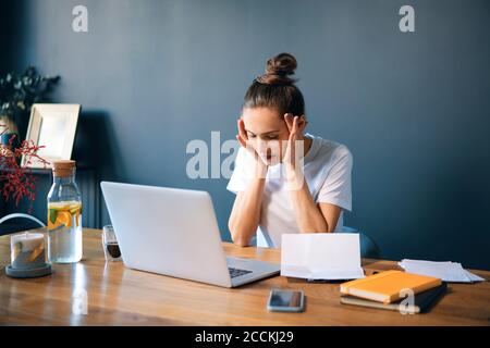 Female entrepreneur with head in hands sitting at desk against wall Stock Photo