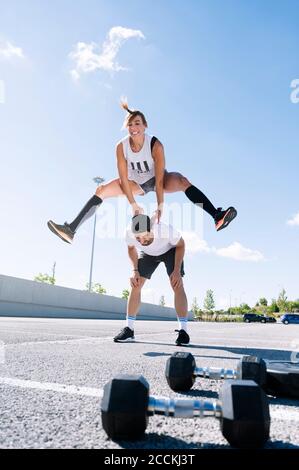 Woman jumping over man on street against sky in city during sunny day Stock Photo