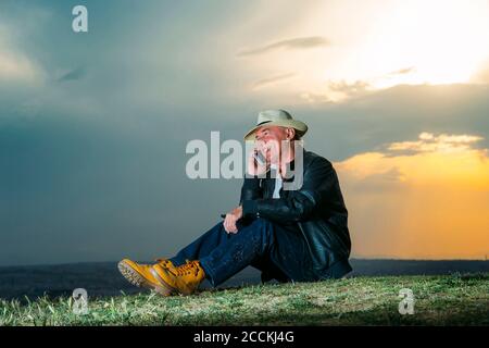 Smiling senior man talking on mobile phone against cloudy sky during sunset Stock Photo