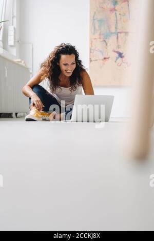 Cheerful mid adult woman using laptop while sitting on floor at home Stock Photo