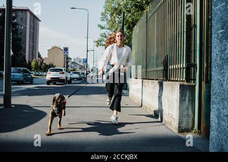 Woman running with dog at sidewalk in city Stock Photo