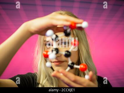 Close-up of young female scientist holding molecule model against grid pattern Stock Photo